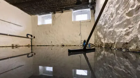Flooded basement with a squeegee on the wet floor and damp, stained walls